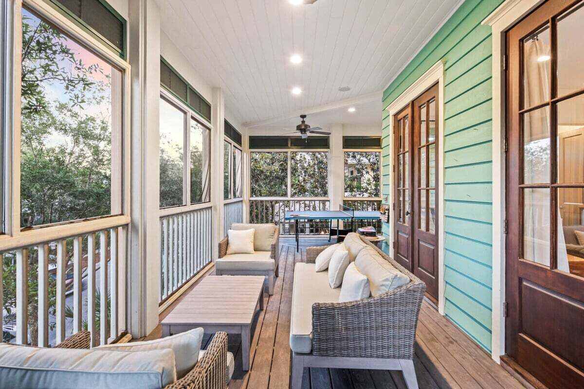 A covered porch with wicker furniture, a table, and a ceiling fan.