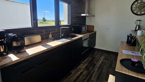 A modern kitchen with dark wood flooring, a large window, and a built-in microwave. - La Maline**** Piscine chauffée et salle de jeux (Sainte-Soulle)
