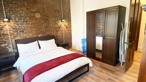 A bedroom with a bed, a ceiling fan, a brick wall, a wardrobe, and a water dispenser.