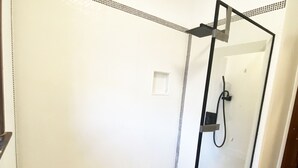 A glass-enclosed shower with a white tiled floor and a small white shelf.