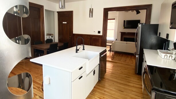 A modern kitchen with a central island, wooden flooring, and stainless steel appliances.