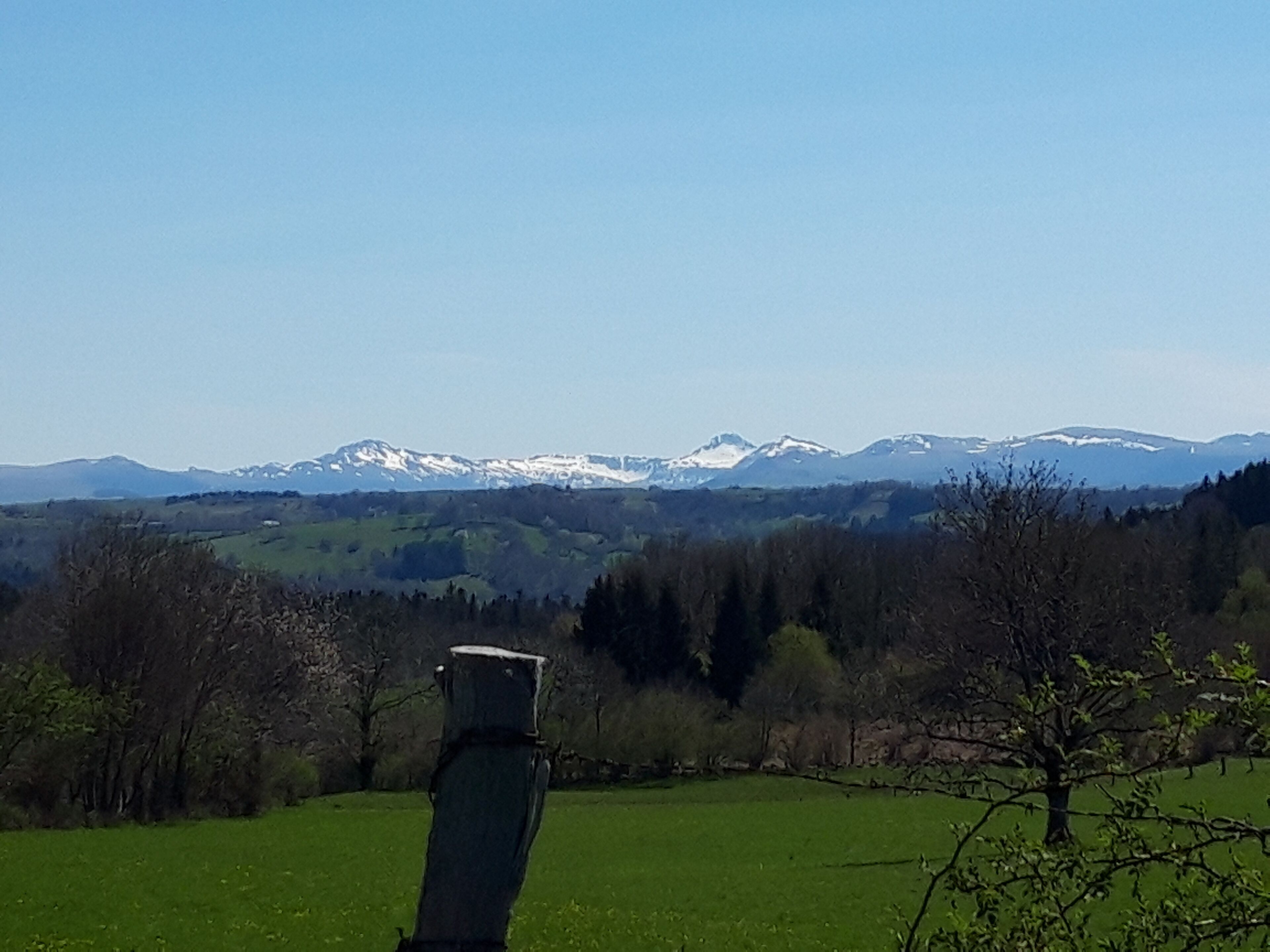 Eine Landschaft mit freiem Blick auf ferne, schneebedeckte Berge, einem grasbewachsen Feld und einer Holzhütte im Vordergrund.