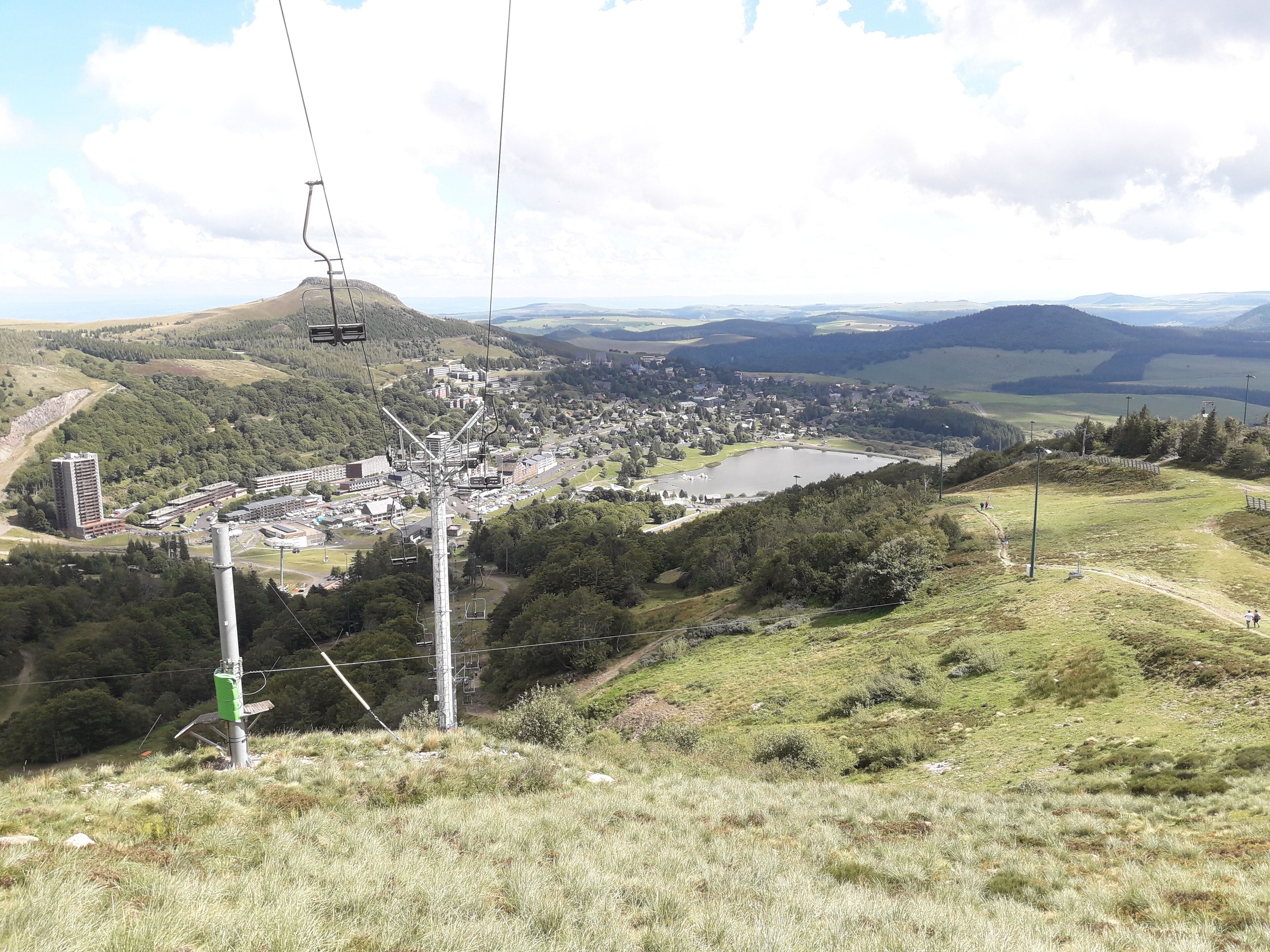 Vista panorámica de un pueblo con un lago, rodeado de colinas y vegetación.