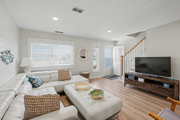 A modern living room with a white sofa, a television on a wooden stand, and a staircase leading to another level.