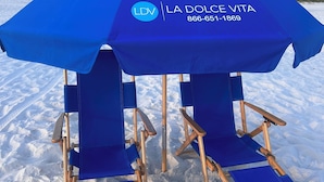 Un ombrellone blu con la scritta "LDV LA DOLOCE VITA" e un numero di telefono.