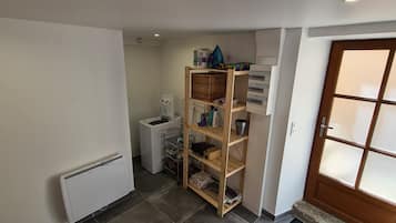 Un couloir avec une étagère en bois, un radiateur blanc, un appareil électroménager blanc et une porte dotée de panneaux en verre dépoli.