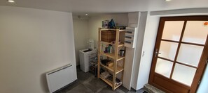 A compact kitchen with a built-in refrigerator, a washing machine, and a wooden shelving unit with various items.