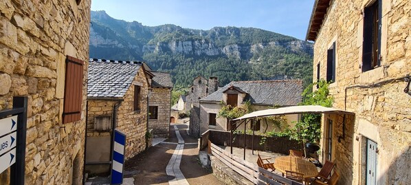 A narrow street with stone buildings, a clear view of a mountain range, and a sign indicating a direction. - Gîte la Cardabelle at Blajoux (Gorges du Tarn Causses)