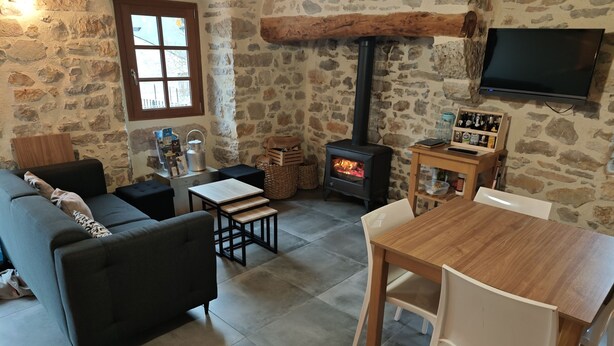 A cozy living room with a stone wall, a fireplace, a sofa, a table, and a TV mounted on the wall.