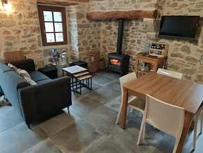 A cozy living room with a stone wall, a fireplace, a sofa, a table, and a TV mounted on the wall.