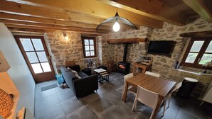 A cozy living room with a stone wall, a fireplace, and a dining area with a wooden table and chairs.