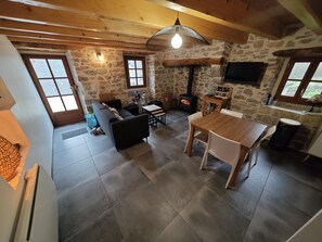 A cozy living room with a stone wall, a fireplace, and a dining area with a wooden table and chairs.
