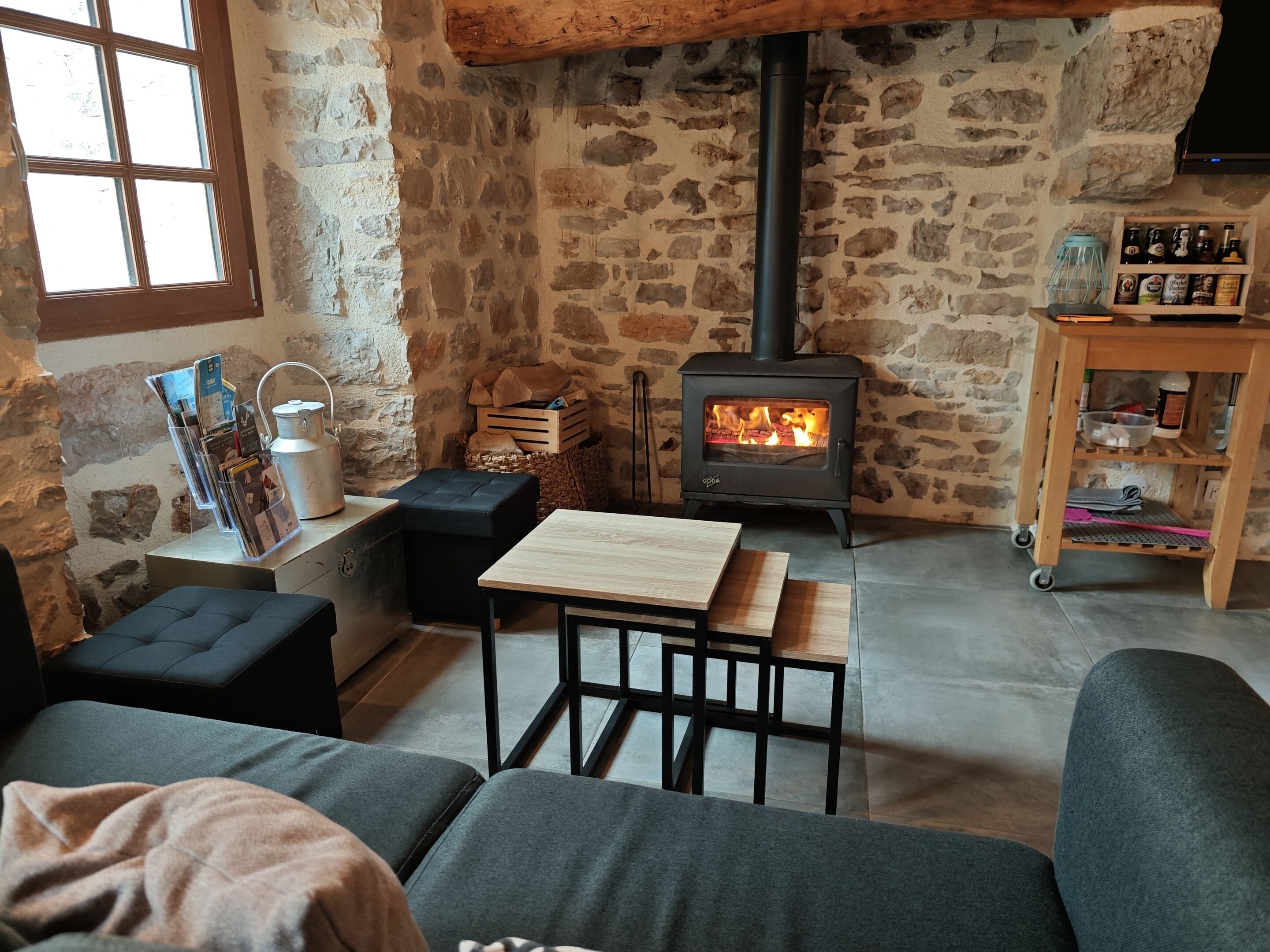 Un salon chaleureux avec un mur en pierre, un poêle à bois, une table en bois et un canapé.