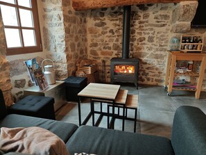 A cozy living room with a stone wall, a wood-burning stove, a wooden table, and a sofa.