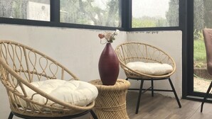 A room with two wicker chairs, a vase, and a view of a house through large windows. - L' Annex ' : charming quiet house with garden close to the beach (Névez)