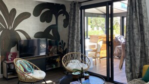 A modern living room with a large TV, wicker furniture, and a view of the outdoors. - L' Annex ' : charming quiet house with garden close to the beach (Névez)