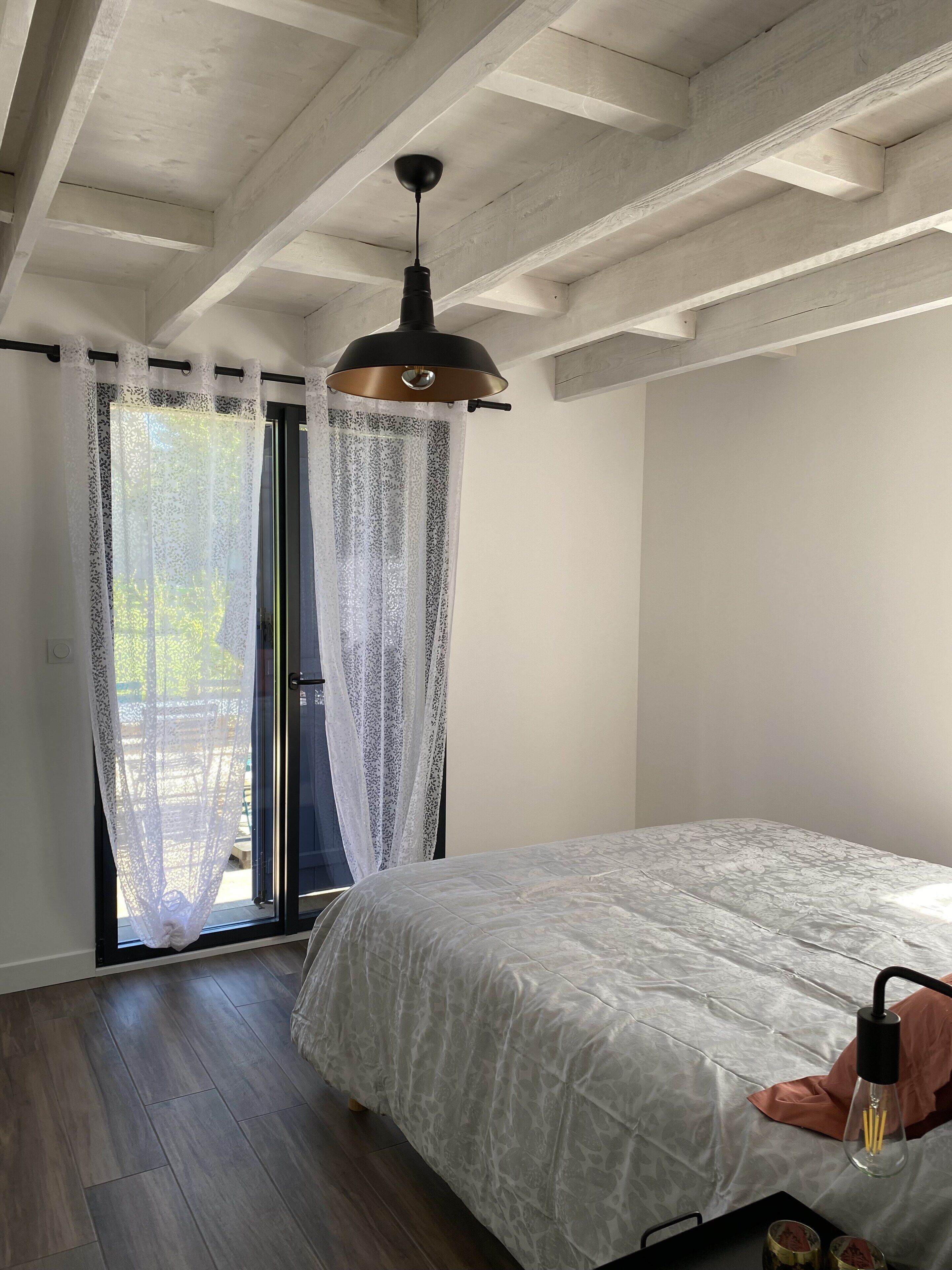 Una camera da letto con un letto, una ventola a soffitto e una finestra con tende leggere.