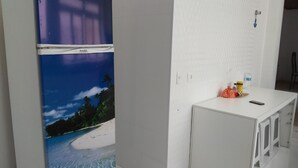 A compact kitchen area with a refrigerator, a small white counter, and a door with a light switch. - Penthouse with its own barbecue near Enseada Beach - Guarujá (Guarujá)