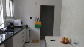 A modern kitchen with white cabinets, a black countertop, a microwave, a coffee maker, and a small refrigerator. - Penthouse with its own barbecue near Enseada Beach - Guarujá (Guarujá)