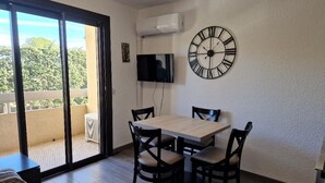 A dining area with a table and chairs, a TV mounted on the wall, and a large clock.
