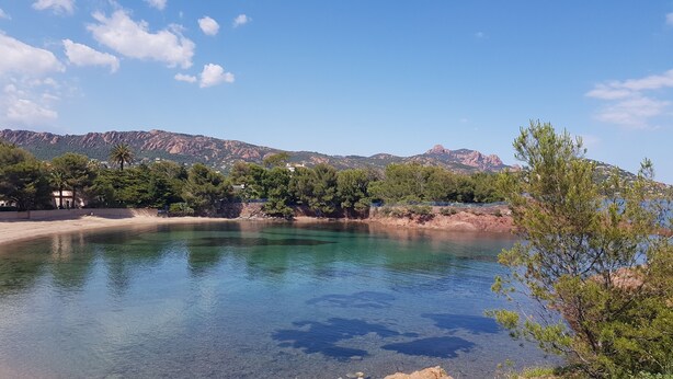 A clear lake with a rocky shoreline, surrounded by trees and mountains in the background.