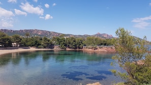 Un lac aux eaux limpides, avec une chaîne de montagnes en arrière-plan, entouré de verdure et de quelques bâtiments.
