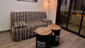 A living room with a striped sofa, two industrial-style barrels, and a sunset painting on the wall.