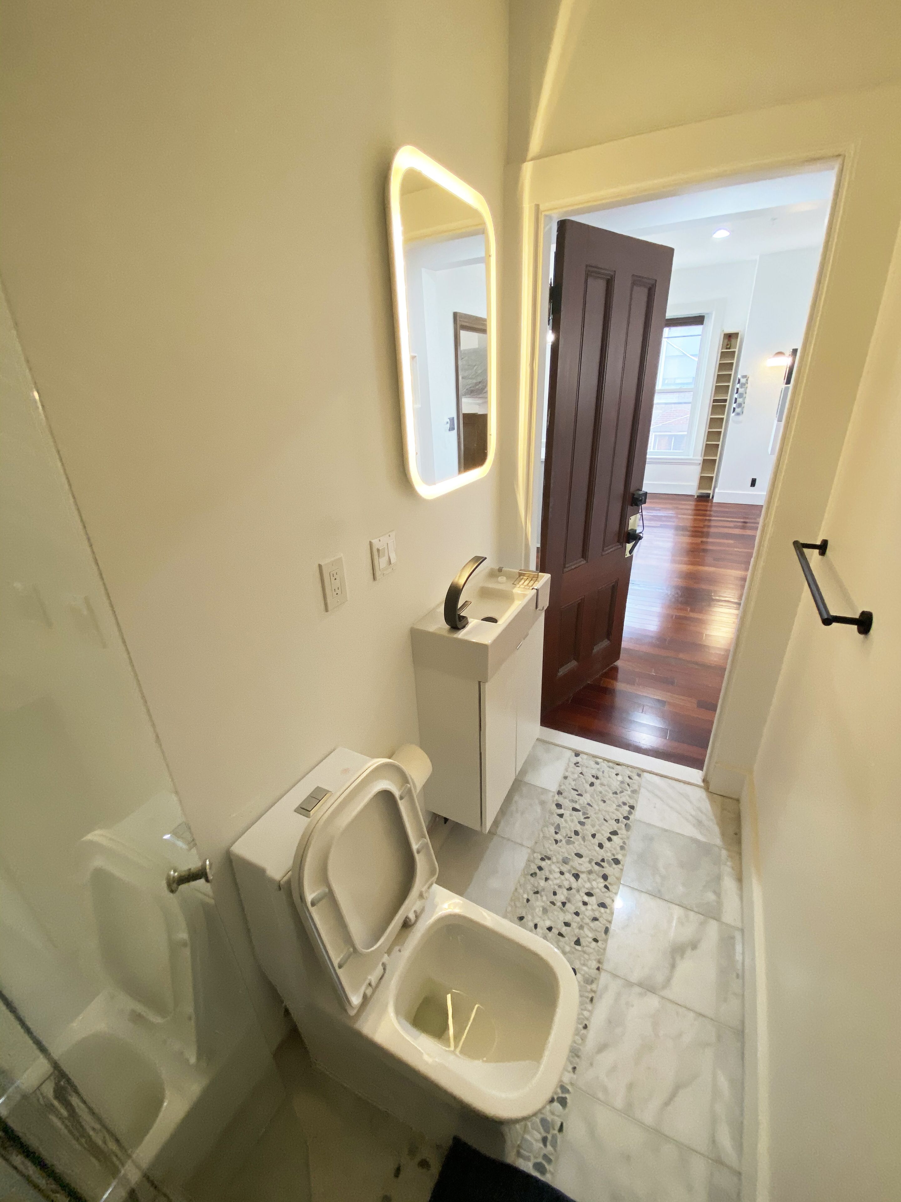 A bathroom with a toilet, sink, and mirror.