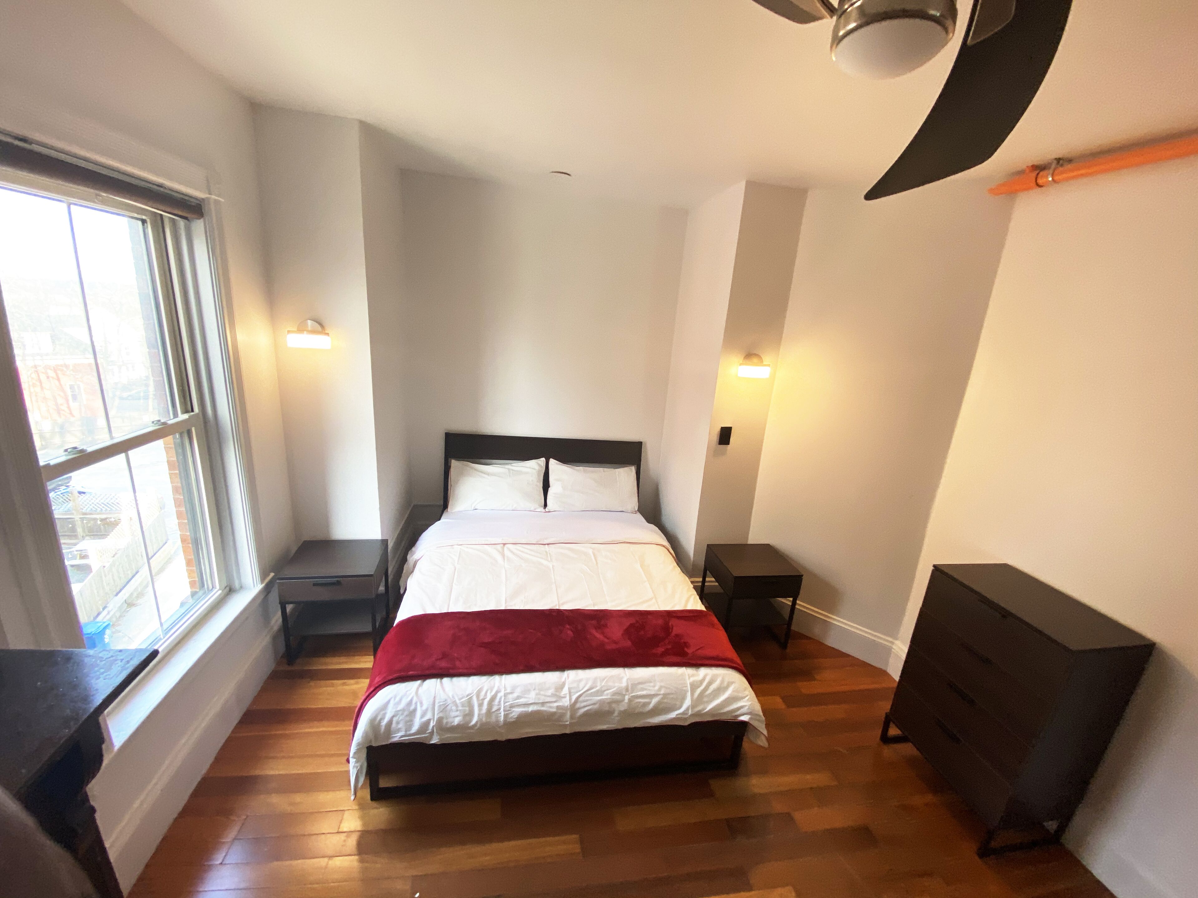 Un dormitorio con cama, ventana, cómoda y ventilador de techo.