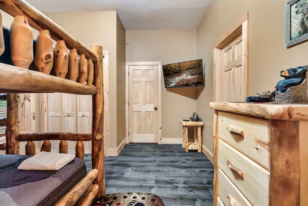 Ein Zimmer mit einem hölzernen Bett, einem kleinen Tisch, einer Kommode und einer Tür zu einem anderen Raum.