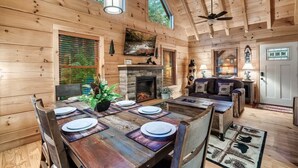 A wooden cabin interior with a dining table, fireplace, and a cozy seating area.