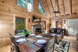 A wooden cabin interior with a dining table, fireplace, and a cozy seating area.