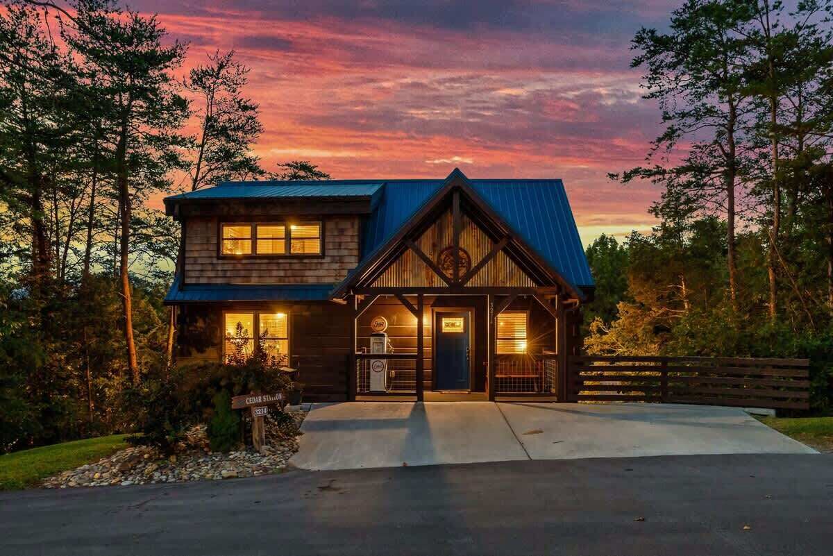 A two-story cabin with a blue roof, a front porch, and a visible garage door.