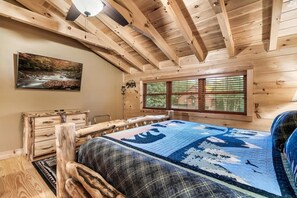Camera da letto in una baita con un letto, una testiera in legno, un quadro, una finestra e un comò di legno.