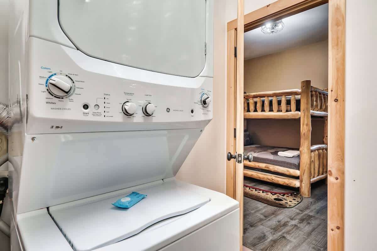 Un espace buanderie comprenant un lave-linge, un lit superposé en bois et une porte donnant sur une pièce.