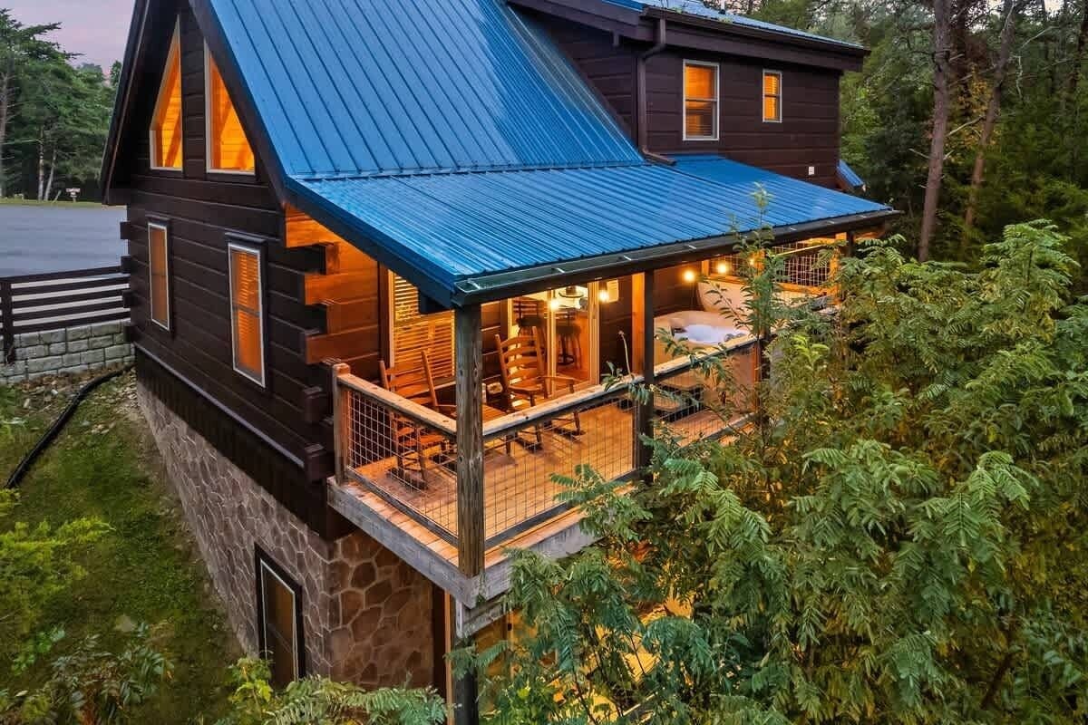 A cabin with a stone foundation, a wooden deck, and a blue metal roof.