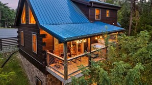 A cabin with a stone foundation, a wooden deck, and a blue metal roof.