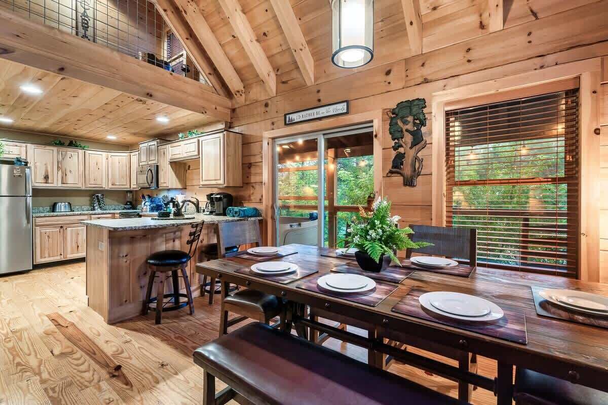 A wooden cabin interior with a dining area, kitchen, and a view of the outdoors.