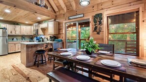 A wooden cabin interior with a dining area, kitchen, and a view of the outdoors.