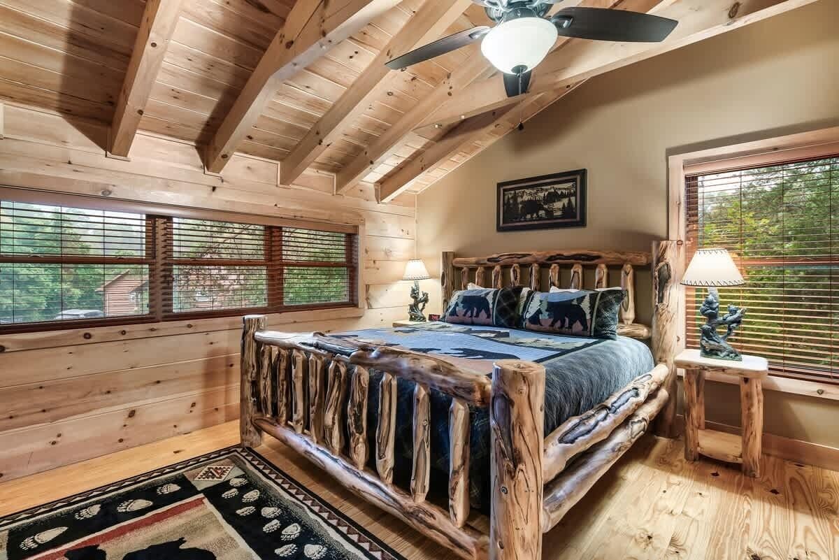 A log cabin bedroom with a wooden bed, a ceiling fan, and large windows.