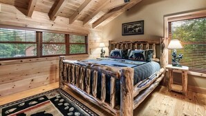 A log cabin bedroom with a wooden bed, a ceiling fan, and large windows.