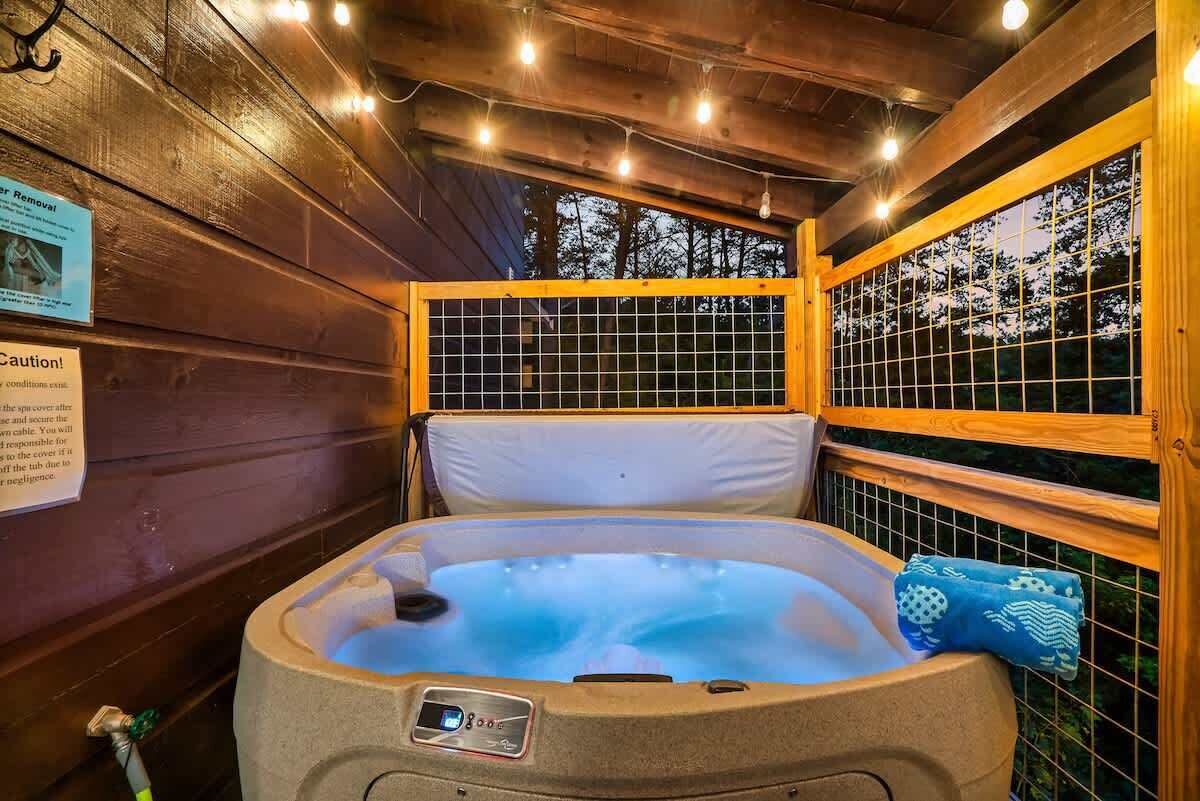 A hot tub in a wooden cabin with a view of trees through a window.