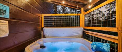 A hot tub in a wooden cabin with a view of trees through a window.