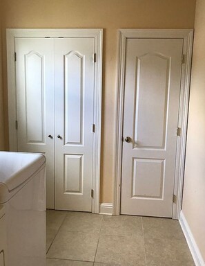 A hallway with two white doors, a laundry area with a washing machine, and beige tiled flooring.