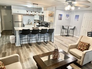 A modern kitchen with a bar area, a dining space with chairs, and a living area with a sofa and a coffee table.