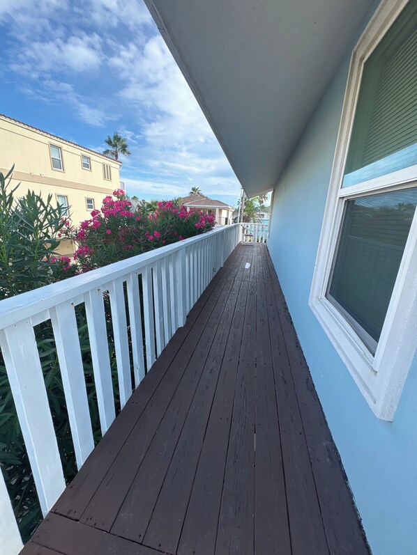 A wooden deck with a white railing, a window, and pink flowers in the background.