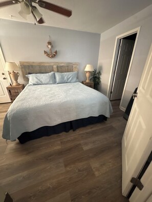 Ein Schlafzimmer mit Bett, Holzboden, Deckenventilator und einer Tür.