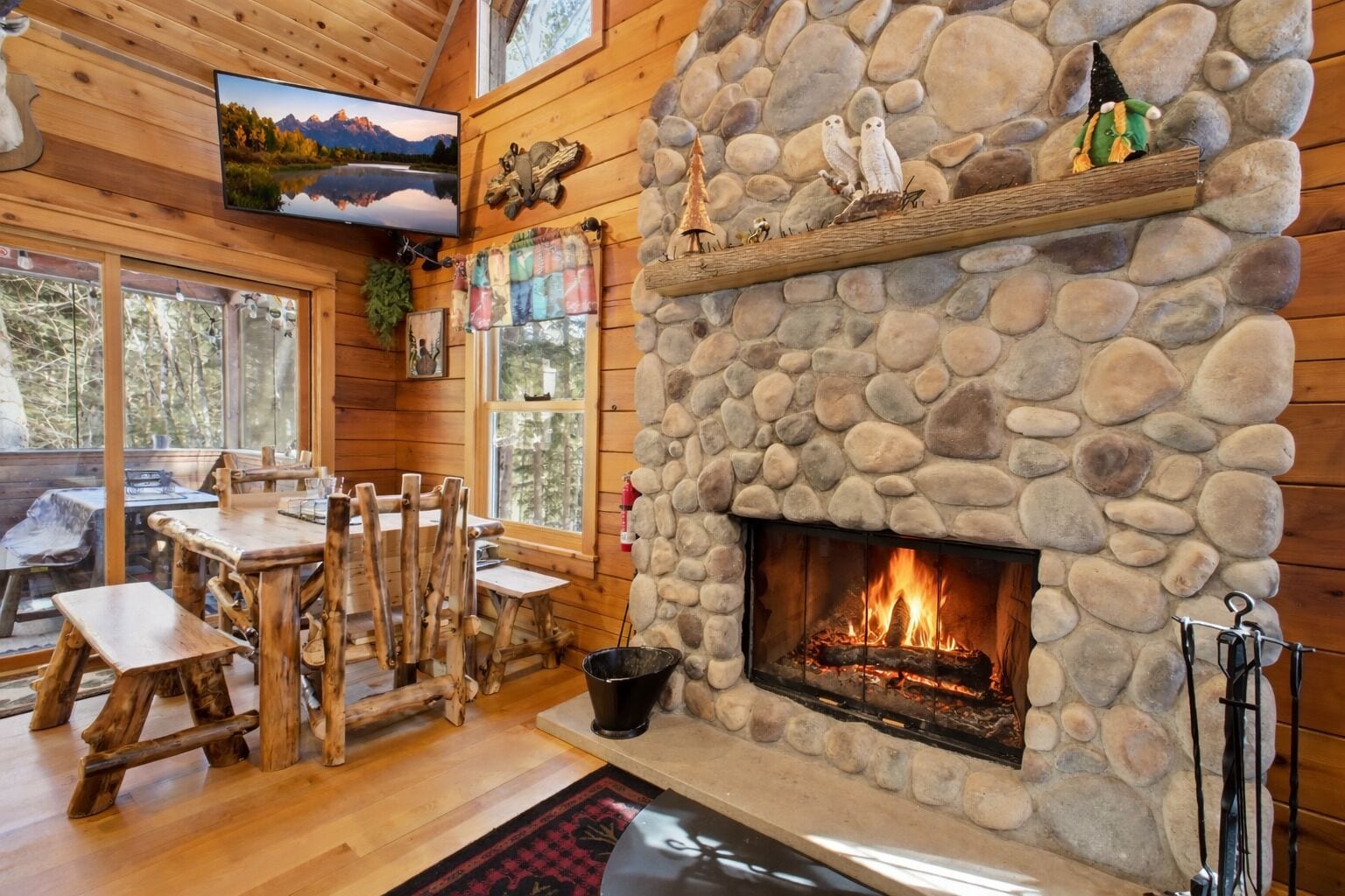 L’intérieur d’un chalet rustique, avec une cheminée en pierre, des meubles en bois et un téléviseur fixé au mur.
