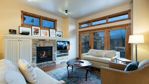 A cozy living room with a fireplace, comfortable seating, and large windows offering a view.