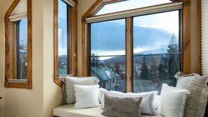 A room with a large window overlooking a snowy landscape, a built-in bench with cushions, and wooden window frames.